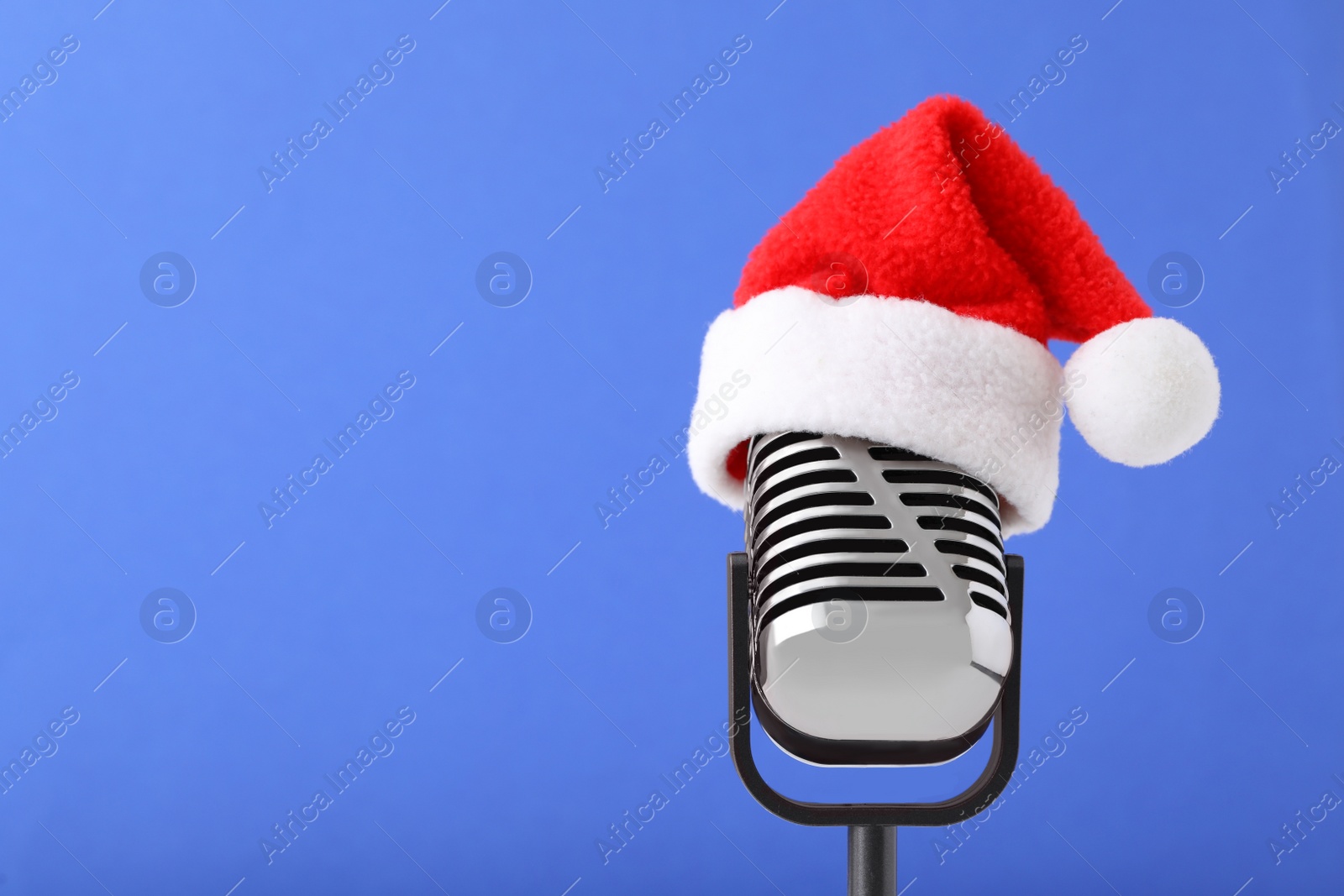 Retro microphone with Santa hat on blue background, space for text. Christmas music Photo of Retro microphone with Santa hat on blue background, space for text. Christmas music