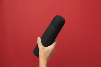 Photo of Woman holding modern black thermos on red background, closeup