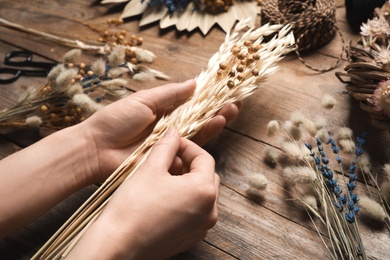 Photo of Florist making bouquet of dried flowers at wooden table, closeup