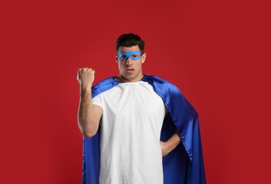 Emotional man wearing superhero cape and mask on red background Photo of Emotional man wearing superhero cape and mask on red background