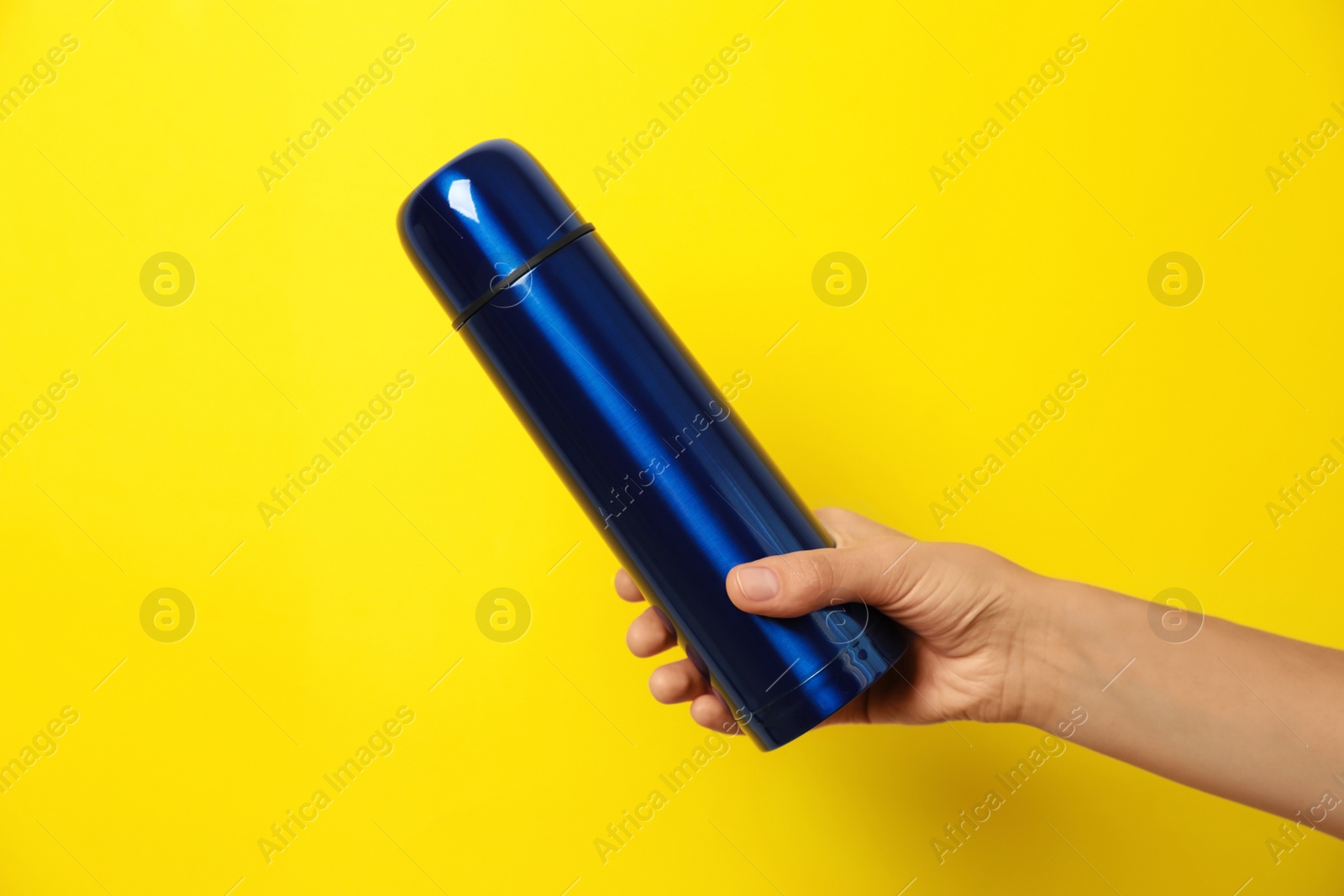 Photo of Woman holding modern blue thermos on yellow background, closeup