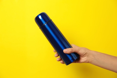 Photo of Woman holding modern blue thermos on yellow background, closeup