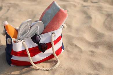 Beach bag with flip flops, towel, sunglasses and sunscreen on sand, space for text Photo of Beach bag with flip flops, towel, sunglasses and sunscreen on sand, space for text