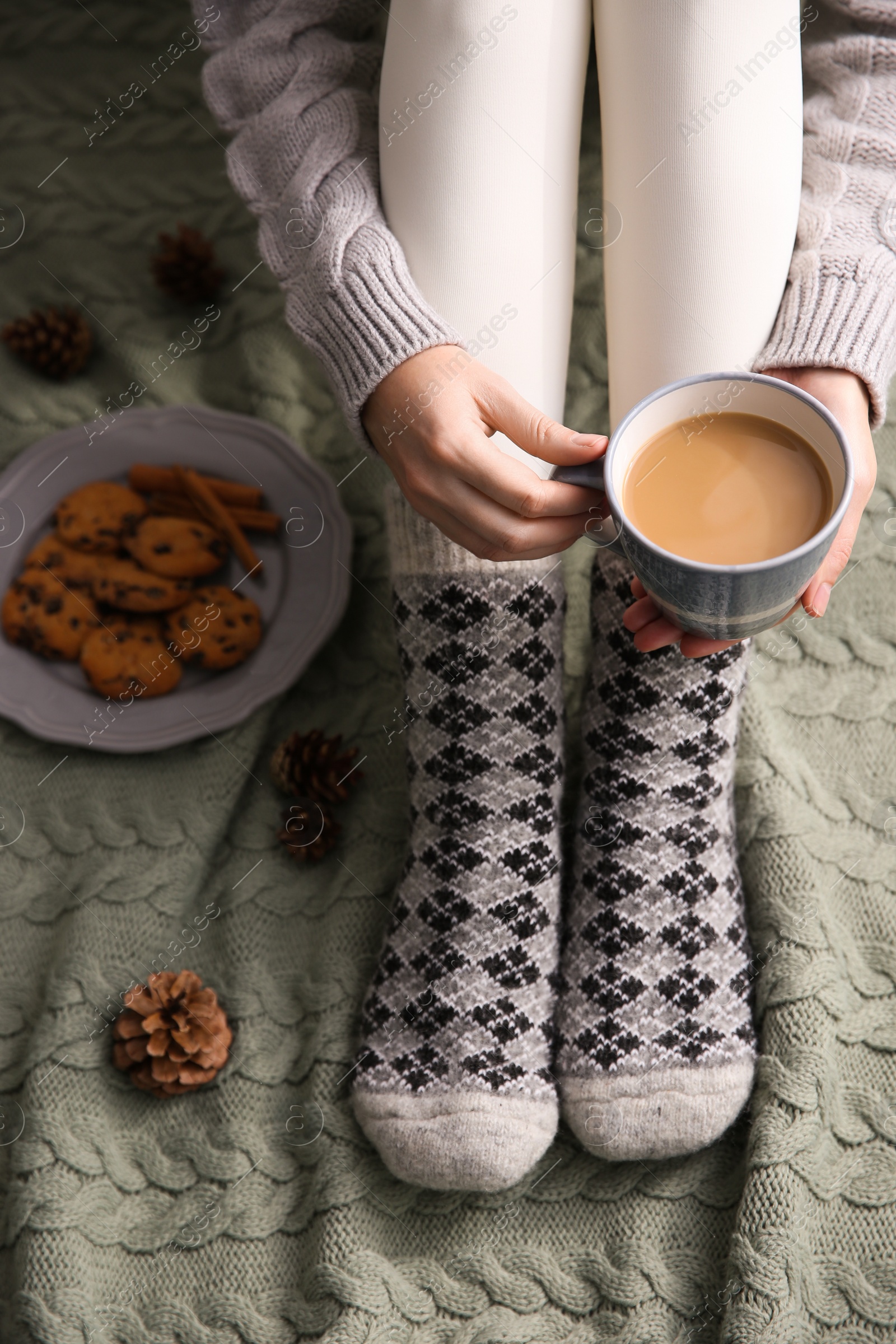 Woman relaxing with cup of hot winter drink on knitted plaid, closeup. Cozy season Photo of Woman relaxing with cup of hot winter drink on knitted plaid, closeup. Cozy season