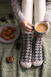 Woman relaxing with cup of hot winter drink on knitted plaid, closeup. Cozy season Photo of Woman relaxing with cup of hot winter drink on knitted plaid, closeup. Cozy season