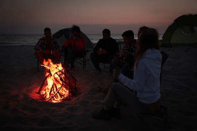 Group of friends gathering around bonfire on beach in evening. Camping season Photo of Group of friends gathering around bonfire on beach in evening. Camping season