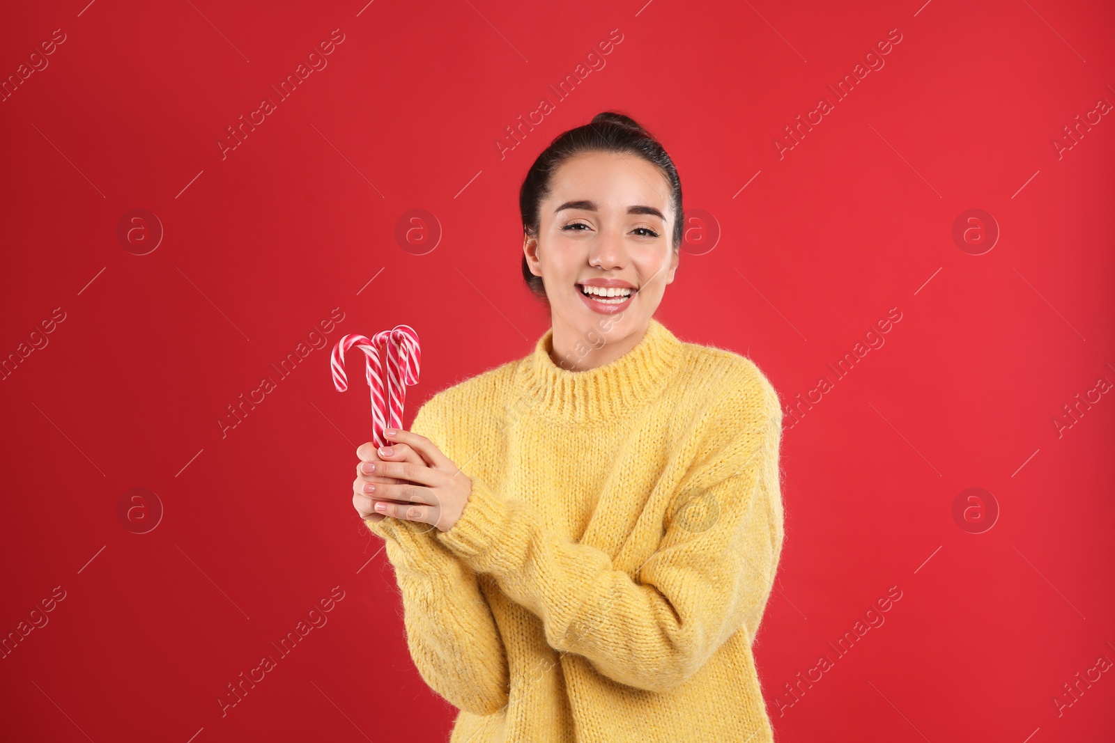 Young woman in yellow sweater holding candy canes on red background. Celebrating Christmas Photo of Young woman in yellow sweater holding candy canes on red background. Celebrating Christmas