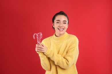 Young woman in yellow sweater holding candy canes on red background. Celebrating Christmas Photo of Young woman in yellow sweater holding candy canes on red background. Celebrating Christmas