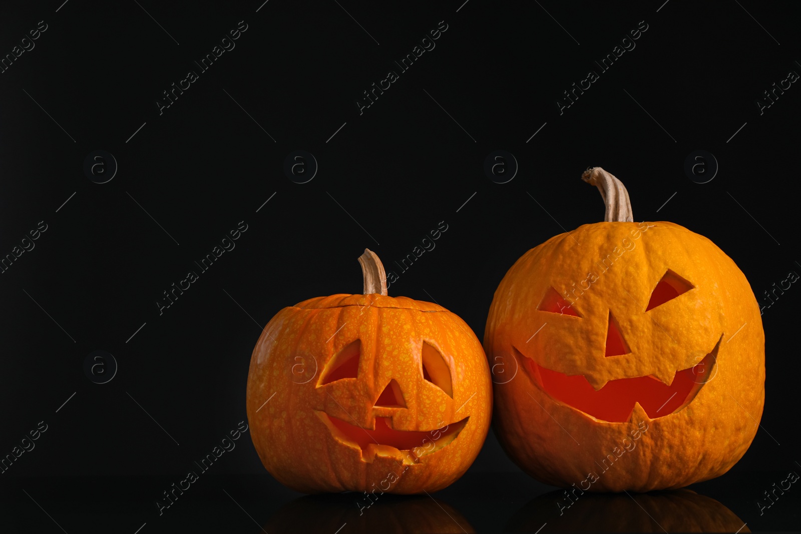 Photo of Pumpkins with scary faces on black background. Halloween traditional decor