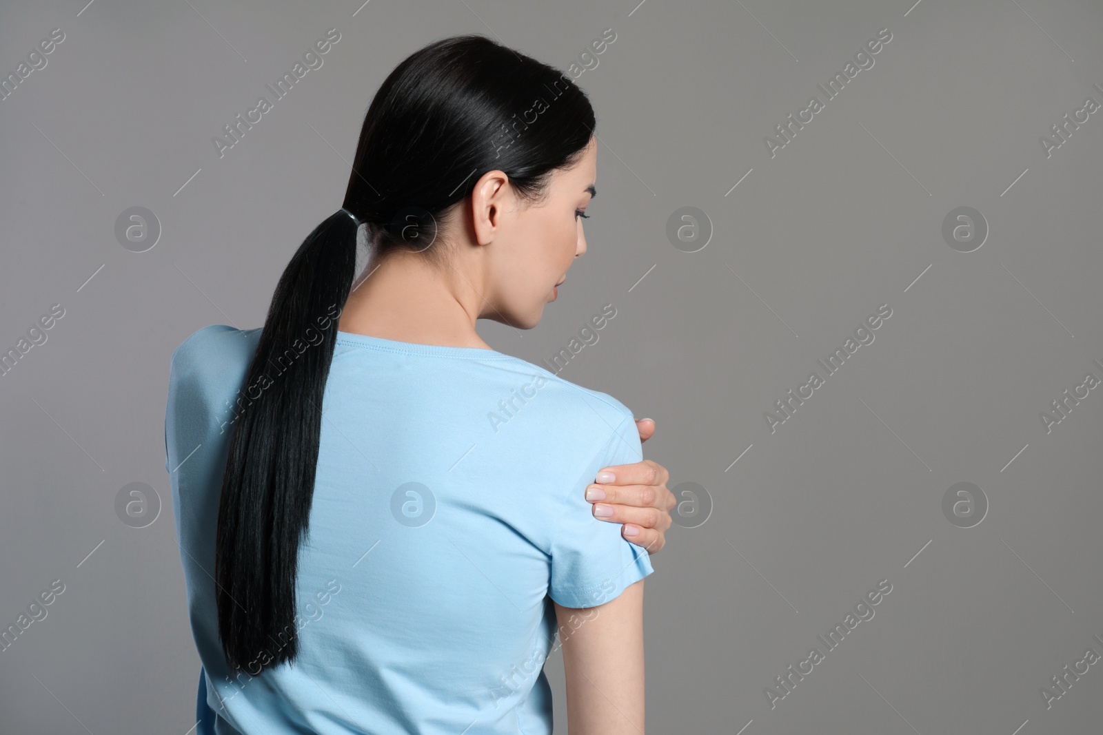 Woman suffering from shoulder pain on beige background, back view Photo of Woman suffering from shoulder pain on beige background, back view