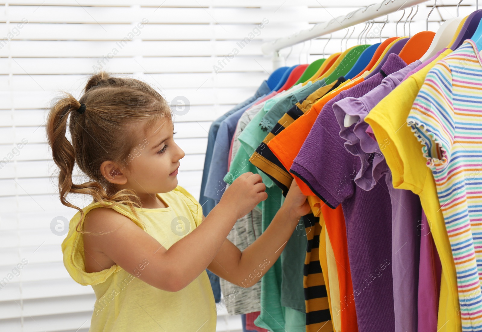 Little girl choosing clothes on rack indoors Photo of Little girl choosing clothes on rack indoors