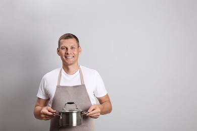 Happy man with cooking pot on light grey background. Space for text Photo of Happy man with cooking pot on light grey background. Space for text