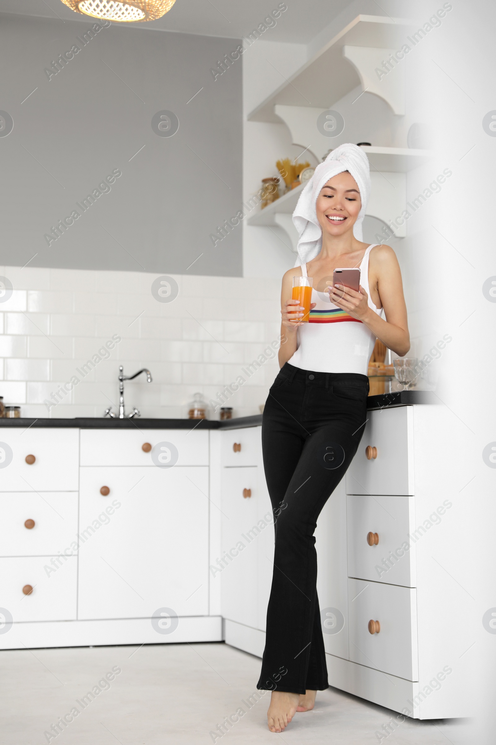 Beautiful young woman with towel, phone and glass of juice in kitchen Photo of Beautiful young woman with towel, phone and glass of juice in kitchen