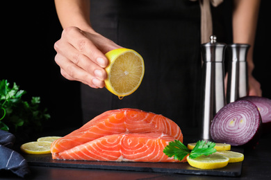 Woman squeezing lemon onto fresh raw salmon at table, closeup. Fish delicacy Photo of Woman squeezing lemon onto fresh raw salmon at table, closeup. Fish delicacy