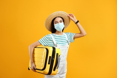 Female tourist in medical mask with suitcase on yellow background. Travelling during coronavirus pandemic Photo of Female tourist in medical mask with suitcase on yellow background. Travelling during coronavirus pandemic