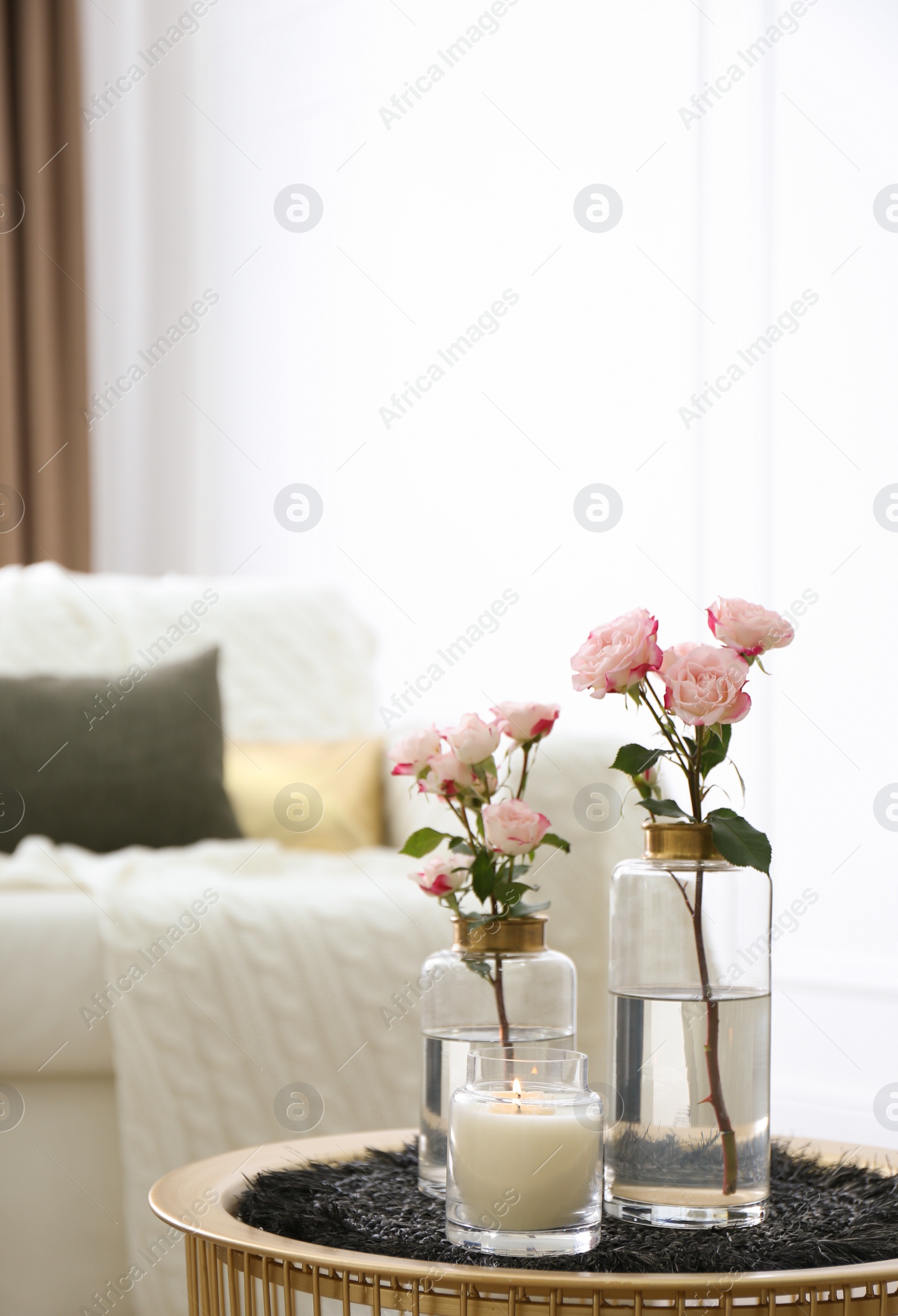 Burning candle and vases with beautiful roses on table indoors, space for text. Interior elements Photo of Burning candle and vases with beautiful roses on table indoors, space for text. Interior elements
