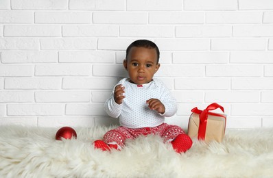 Cute little African American baby with Christmas gift and ball on floor Image of Cute little African American baby with Christmas gift and ball on floor