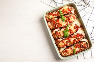 Baked eggplant with tomatoes, cheese and basil in dishware on white wooden table, flat lay. Space for text Photo of Baked eggplant with tomatoes, cheese and basil in dishware on white wooden table, flat lay. Space for text