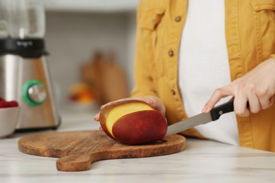 Woman preparing mango for tasty smoothie at white marble table in kitchen, closeup Photo of Woman preparing mango for tasty smoothie at white marble table in kitchen, closeup