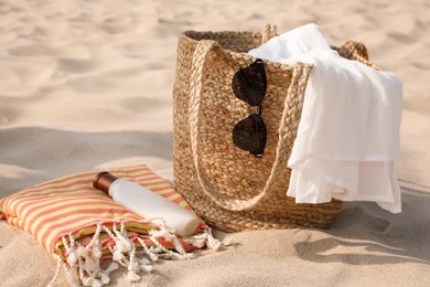 Beach bag, towel, blanket, sunglasses and sunscreen on sand Photo of Beach bag, towel, blanket, sunglasses and sunscreen on sand