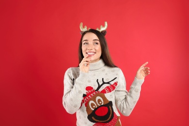Young woman in Christmas sweater and deer headband on red background Photo of Young woman in Christmas sweater and deer headband on red background