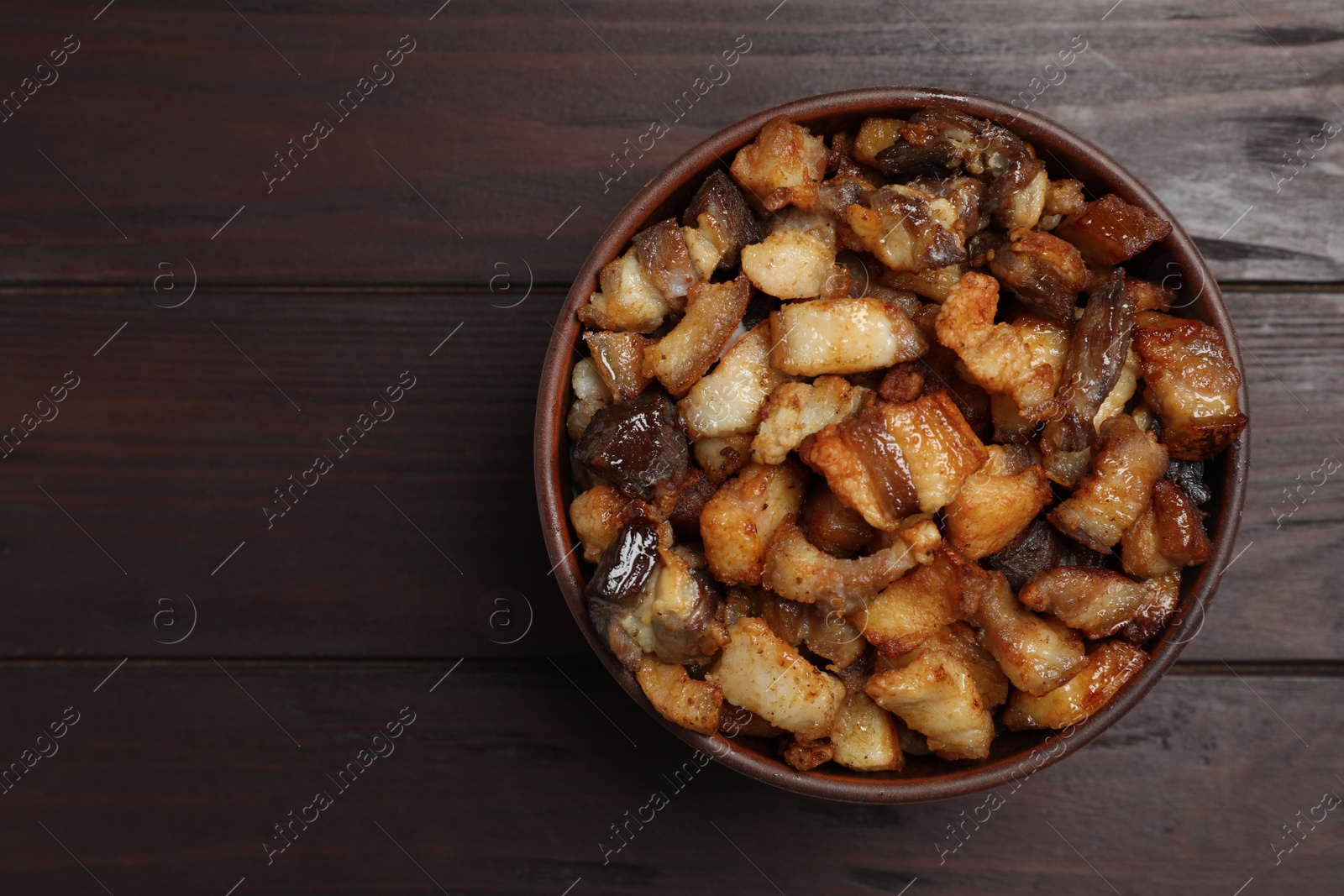 Tasty fried cracklings in bowl on wooden table, top view with space for text. Cooked pork lard Photo of Tasty fried cracklings in bowl on wooden table, top view with space for text. Cooked pork lard