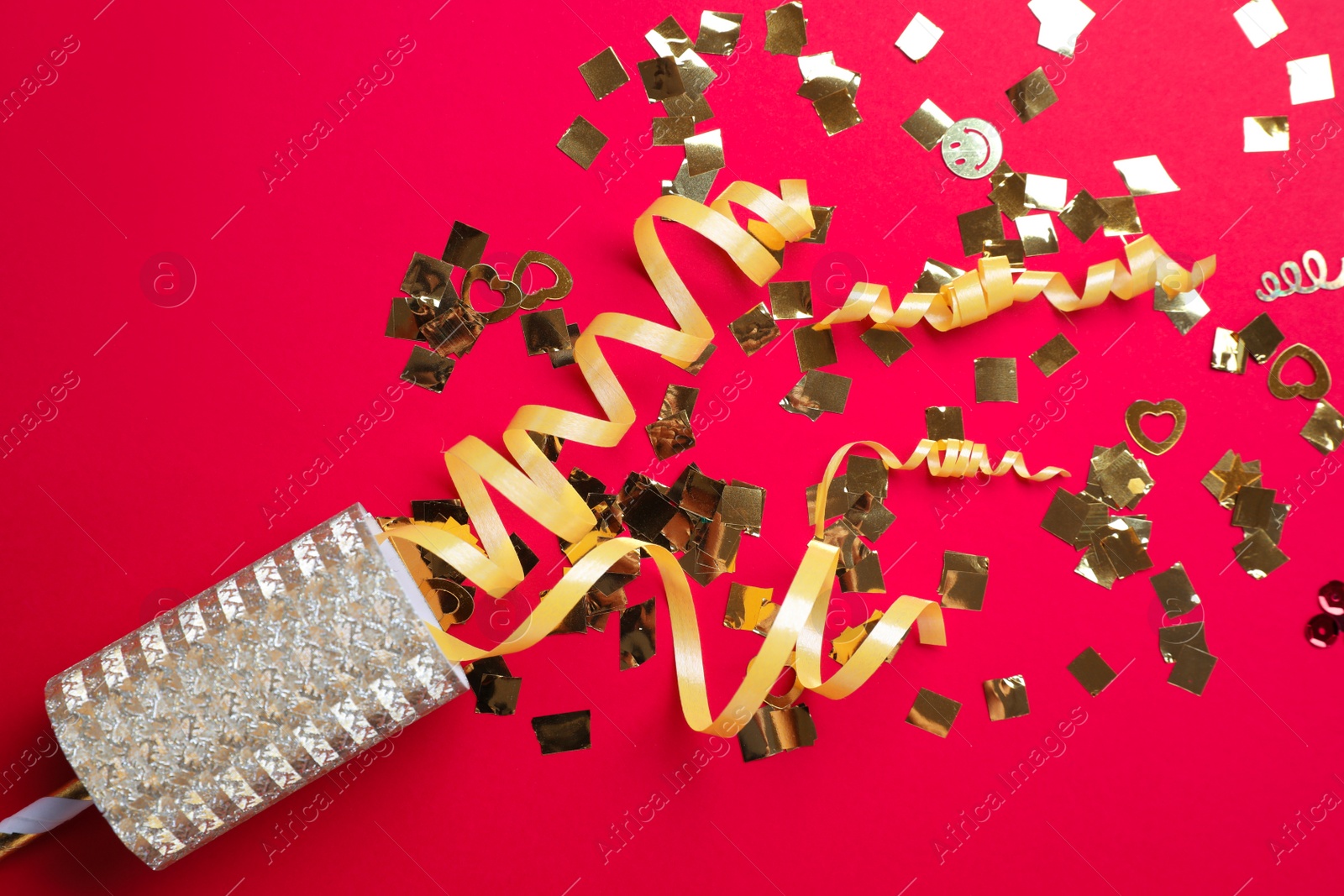 Golden confetti and streamers with party cracker on red background, top view Photo of Golden confetti and streamers with party cracker on red background, top view