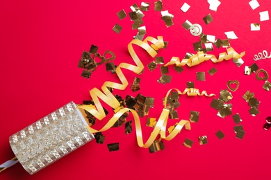 Golden confetti and streamers with party cracker on red background, top view Photo of Golden confetti and streamers with party cracker on red background, top view