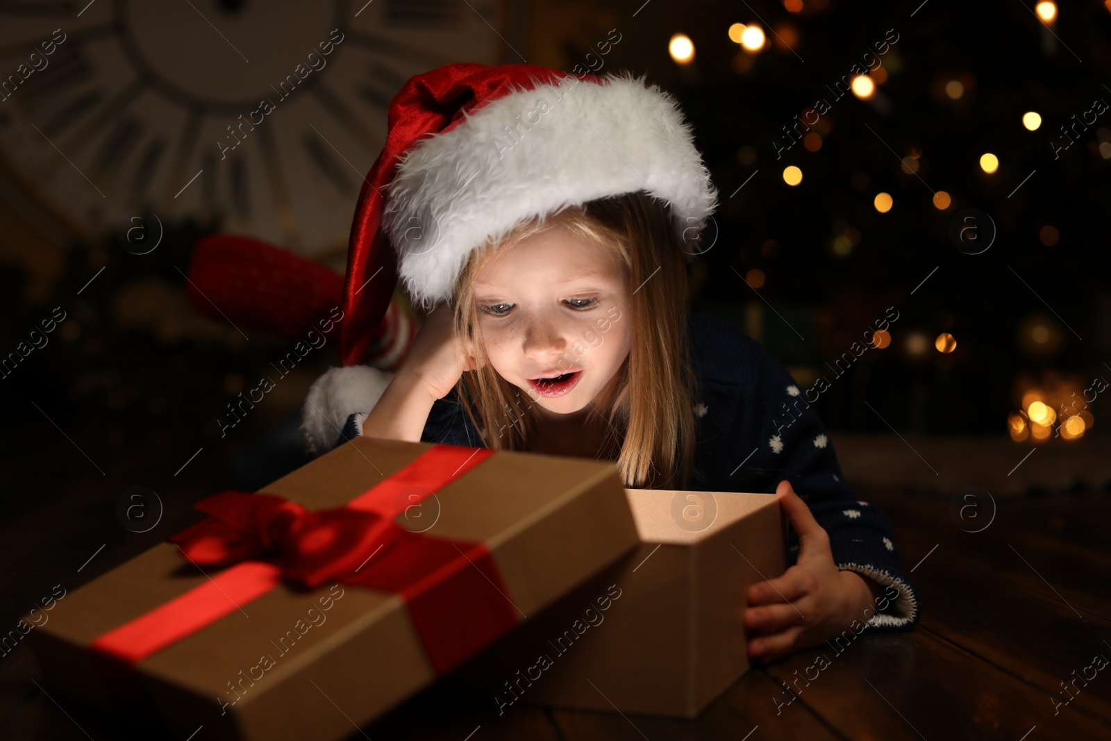 Cute child opening magic gift box near Christmas tree at night Photo of Cute child opening magic gift box near Christmas tree at night