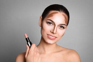 Young woman with contouring lines on her face against grey background. Professional makeup products Photo of Young woman with contouring lines on her face against grey background. Professional makeup products