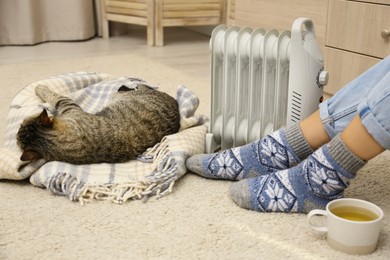 Young woman and cute tabby cat near electric heater at home, closeup Image of Young woman and cute tabby cat near electric heater at home, closeup