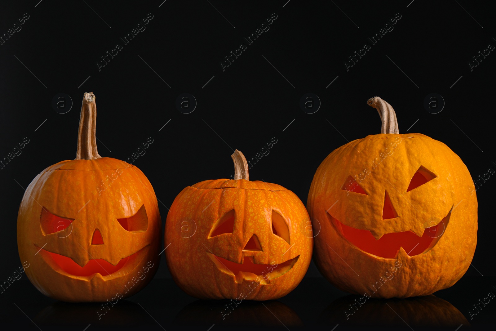 Photo of Pumpkins with scary faces on black background. Halloween traditional decor