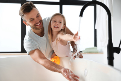 Father with his cute little daughter filling tub in bathroom Photo of Father with his cute little daughter filling tub in bathroom