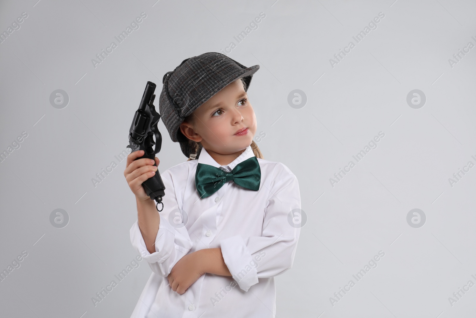 Cute little detective with revolver on grey background Photo of Cute little detective with revolver on grey background