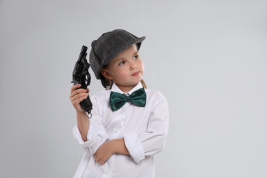 Cute little detective with revolver on grey background Photo of Cute little detective with revolver on grey background
