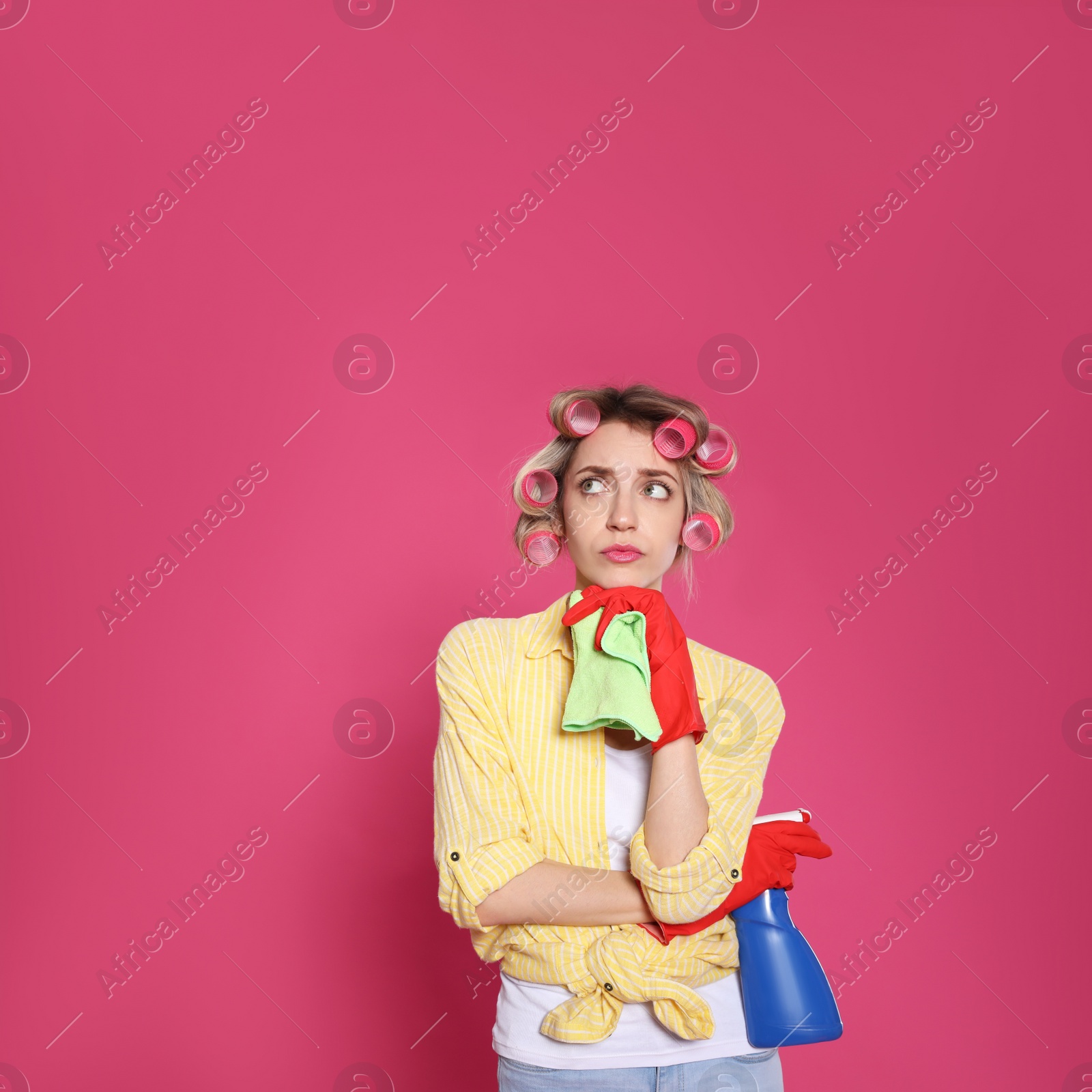 Young housewife with detergent and rag on pink background Photo of Young housewife with detergent and rag on pink background