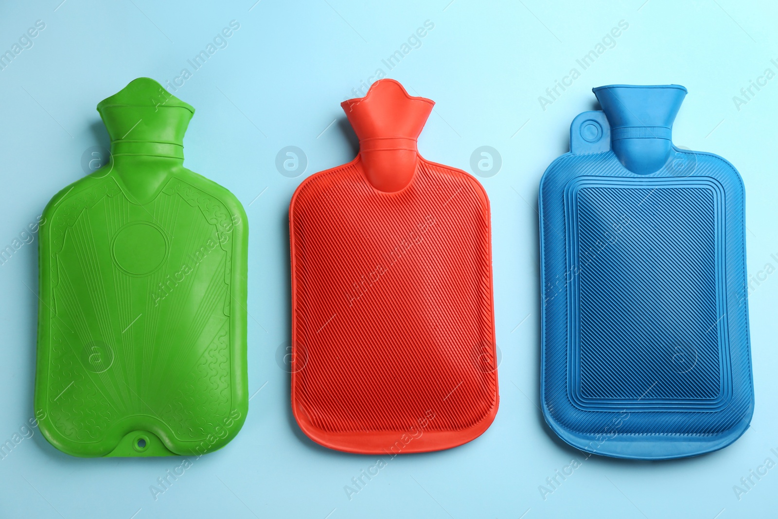 Photo of Hot water bottles on light blue background, flat lay
