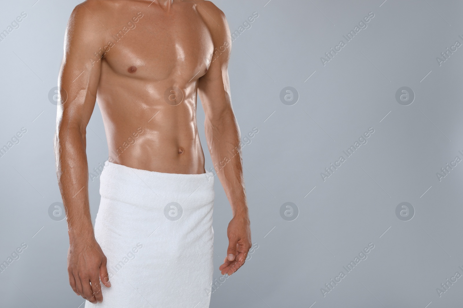 Photo of Shirtless man with slim body and towel wrapped around his hips on grey background, closeup. Space for text
