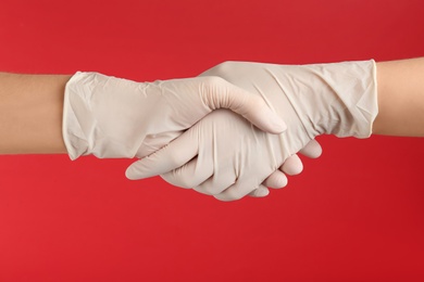 People in medical gloves shaking hands on red background, closeup Photo of People in medical gloves shaking hands on red background, closeup
