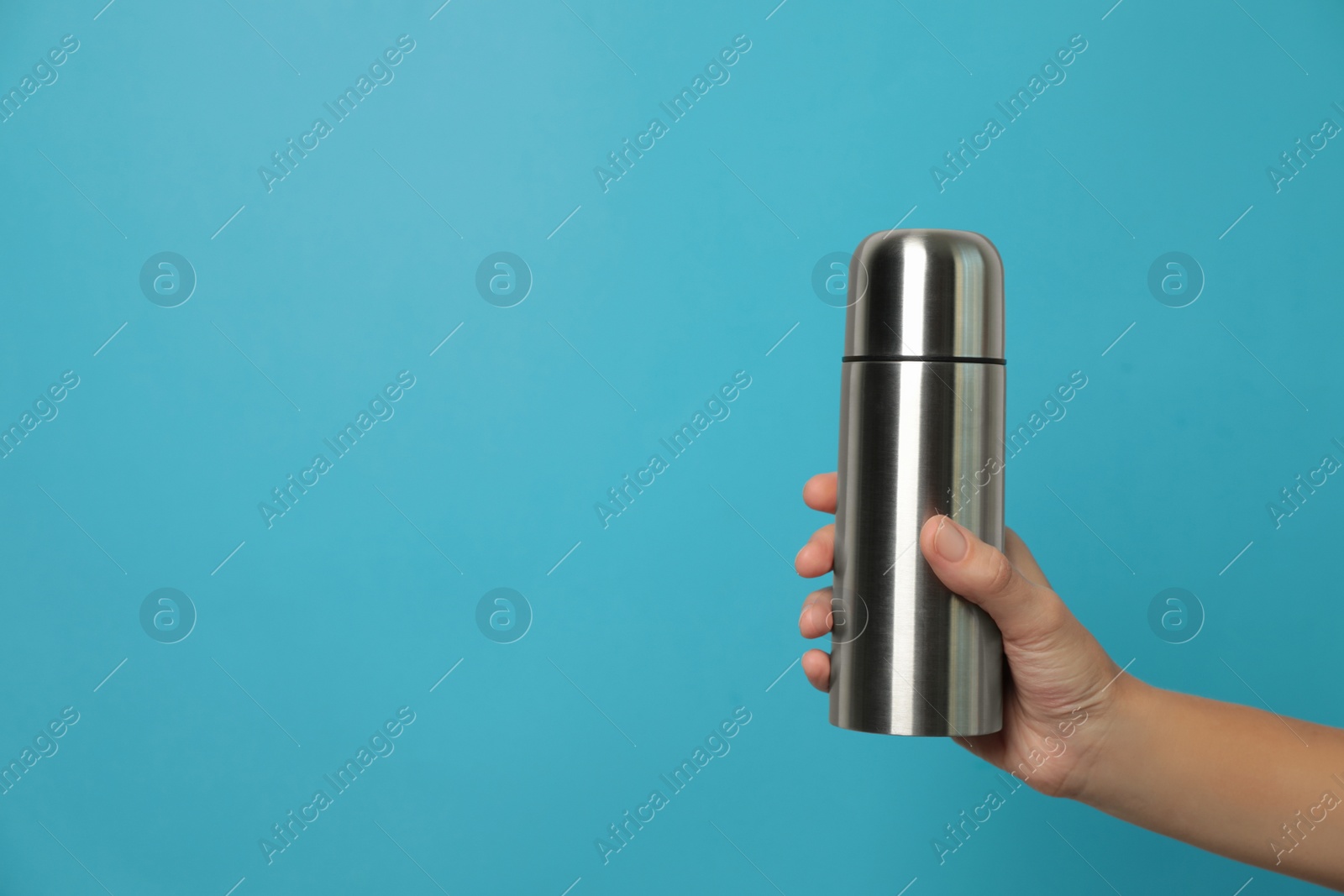 Photo of Woman holding modern thermos on light blue background, closeup. Space for text