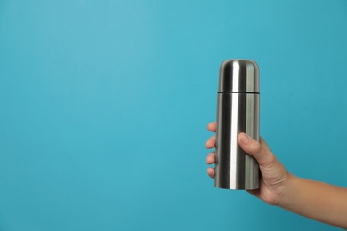 Woman holding modern thermos on light blue background, closeup. Space for text Photo of Woman holding modern thermos on light blue background, closeup. Space for text