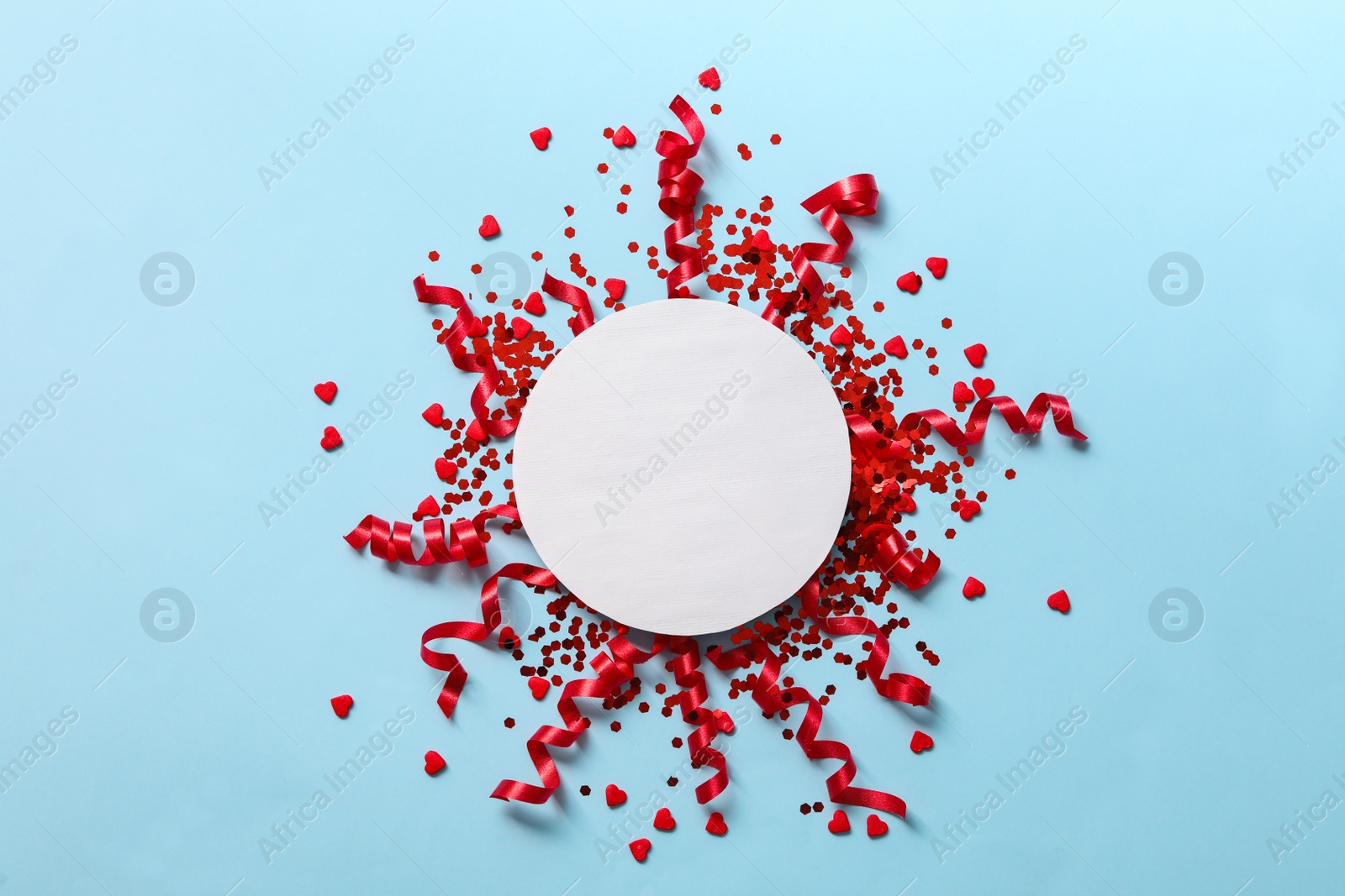 Shiny red serpentine streamers with confetti and blank card on light blue background, flat lay. Space for text Photo of Shiny red serpentine streamers with confetti and blank card on light blue background, flat lay. Space for text