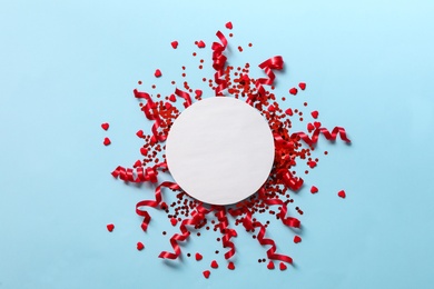 Shiny red serpentine streamers with confetti and blank card on light blue background, flat lay. Space for text Photo of Shiny red serpentine streamers with confetti and blank card on light blue background, flat lay. Space for text