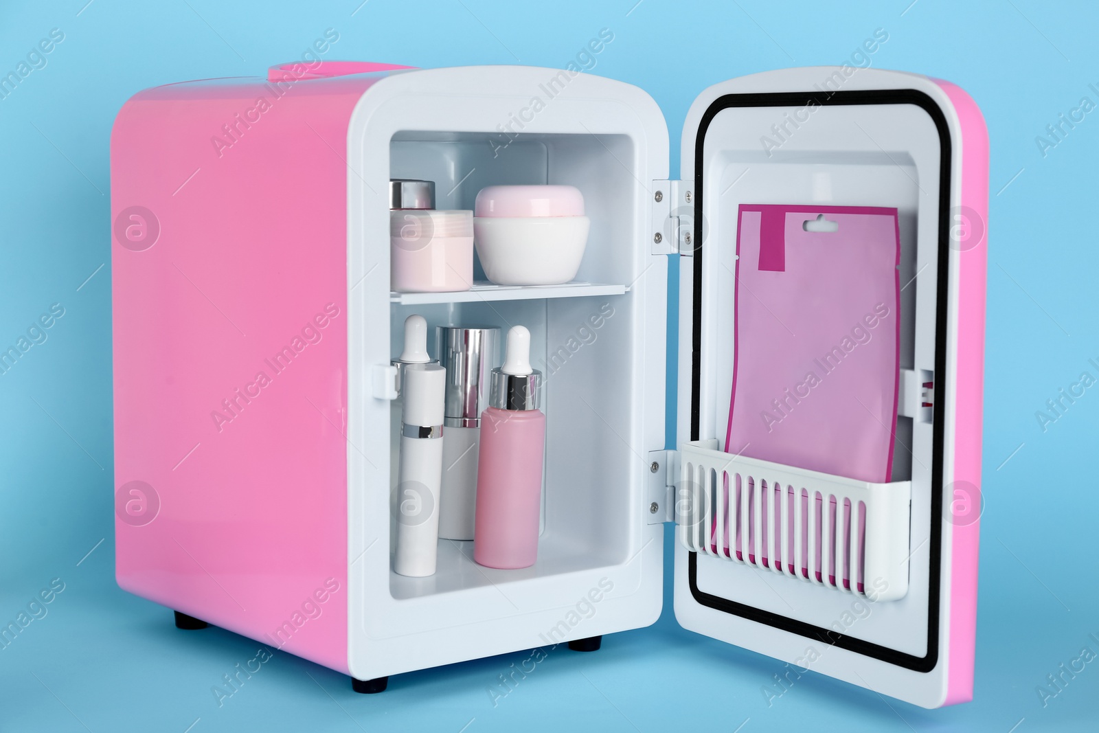 Pink cosmetics refrigerator with skin care products on light blue background Photo of Pink cosmetics refrigerator with skin care products on light blue background