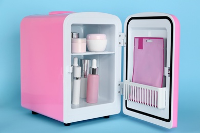 Pink cosmetics refrigerator with skin care products on light blue background Photo of Pink cosmetics refrigerator with skin care products on light blue background