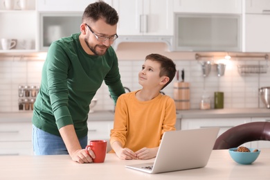 Photo of Little boy and his dad using laptop in kitchen