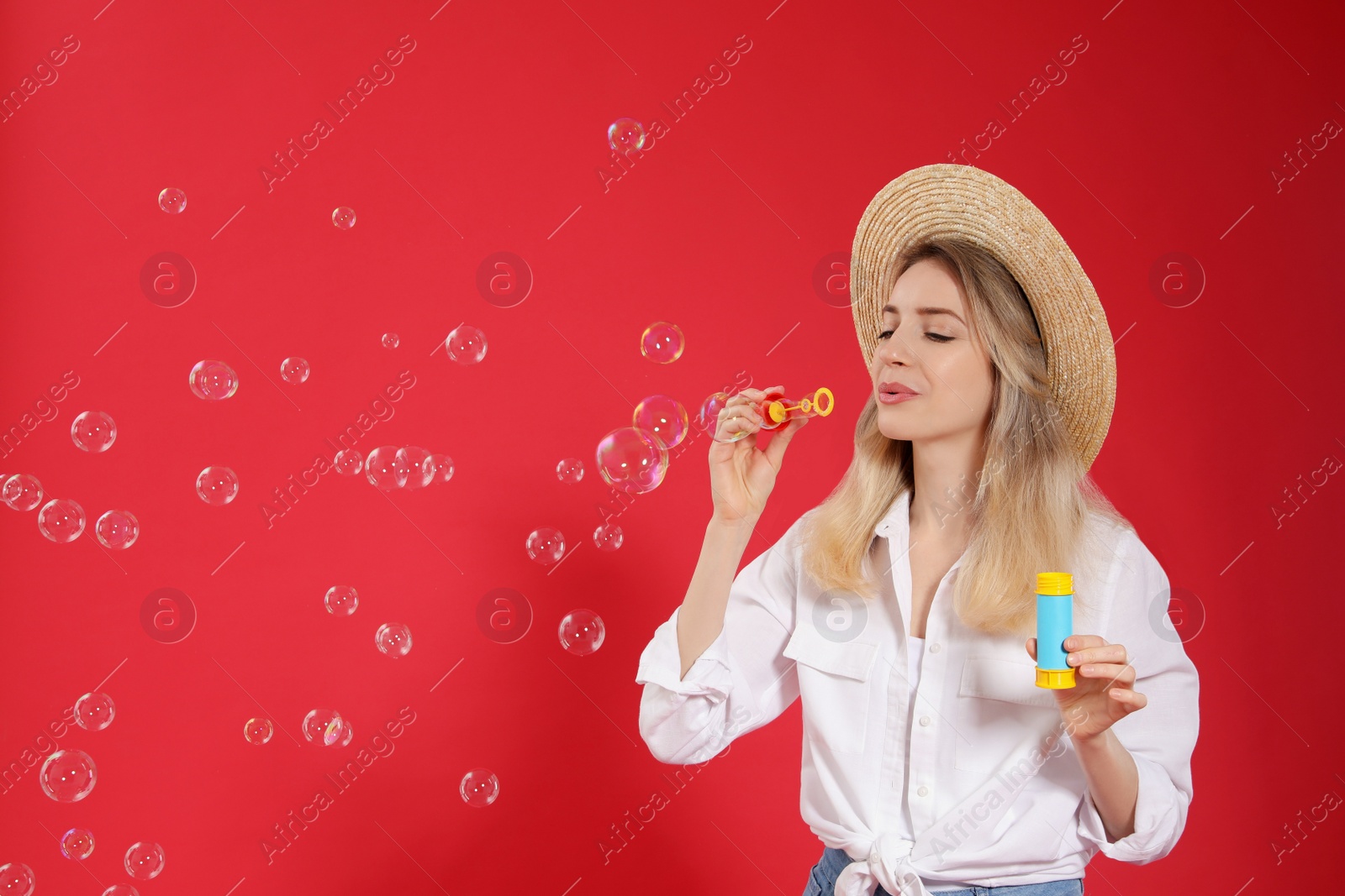 Young woman blowing soap bubbles on red background, space for text Photo of Young woman blowing soap bubbles on red background, space for text