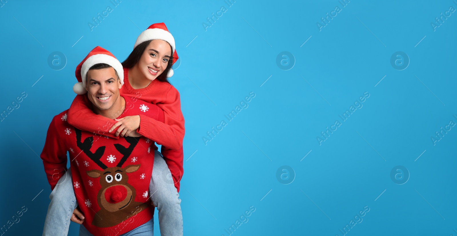 Couple in Christmas sweaters and Santa hats on blue background, space for text Photo of Couple in Christmas sweaters and Santa hats on blue background, space for text
