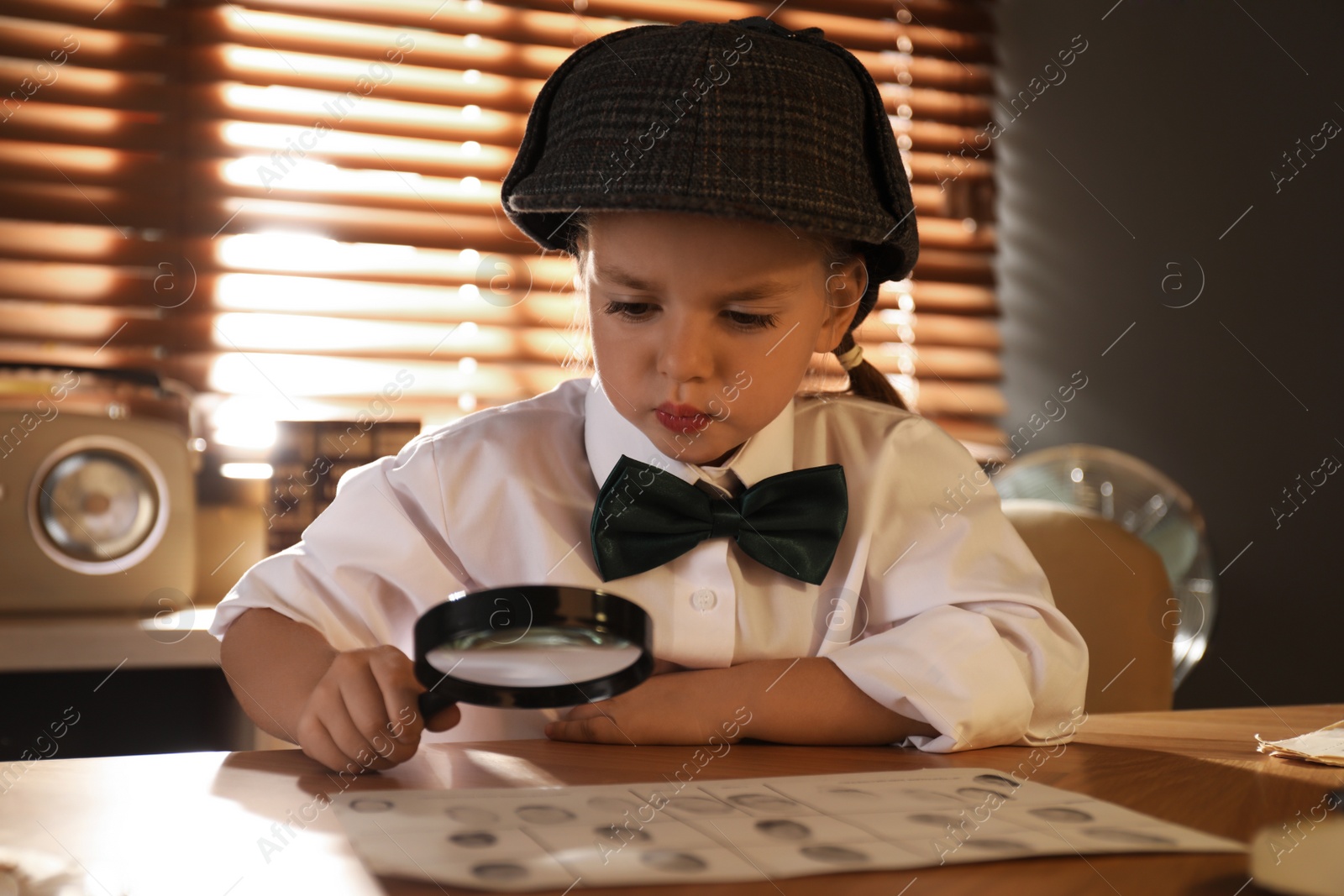 Cute little detective exploring fingerprints with magnifying glass at table in office Photo of Cute little detective exploring fingerprints with magnifying glass at table in office