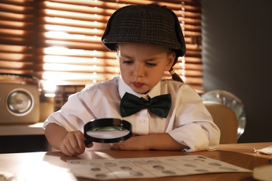 Cute little detective exploring fingerprints with magnifying glass at table in office Photo of Cute little detective exploring fingerprints with magnifying glass at table in office